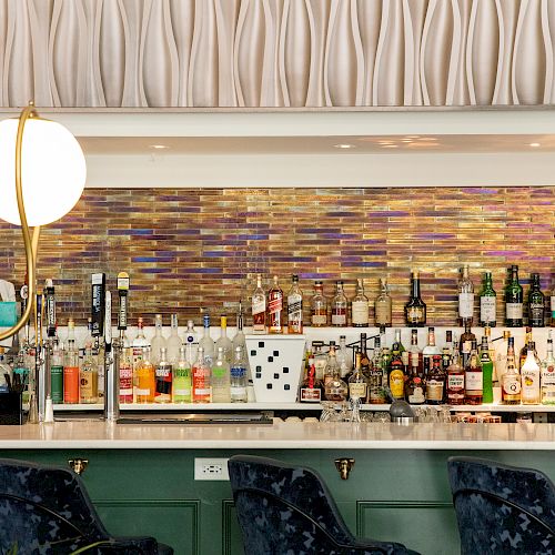 A decorated bar with a wide variety of bottles and a modern wall design, with two bar stools in front.