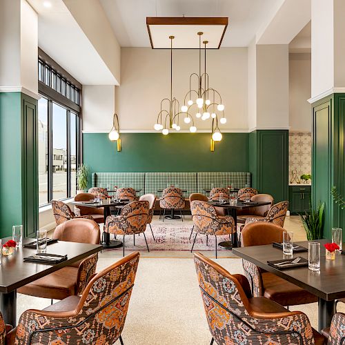 A stylish, modern restaurant with green accents, patterned chairs, elegant lighting, and large windows allowing natural light. Tables are set for dining.