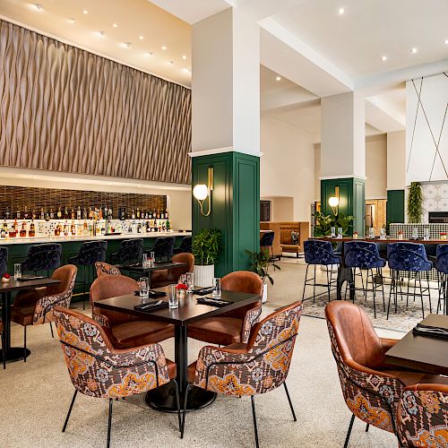 The image shows a modern restaurant interior featuring a bar area, dining tables, and chairs with colorful patterns, and contemporary decor accents.