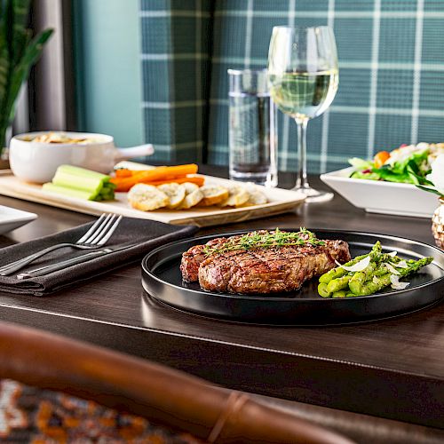 This image shows a table set with a steak, vegetables, salad, bread with dips, and various drinks, creating a fine dining scene.