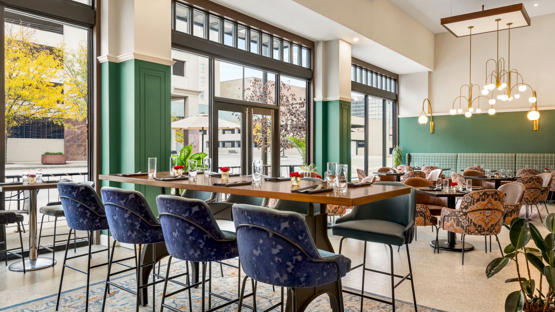 A modern, airy restaurant with large windows, stylish seating, elegant lighting fixtures, and a mix of high and low tables, offering a cozy ambiance.