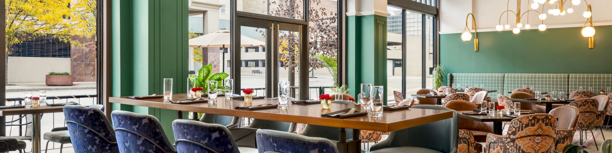 A modern, airy restaurant with large windows, stylish seating, elegant lighting fixtures, and a mix of high and low tables, offering a cozy ambiance.